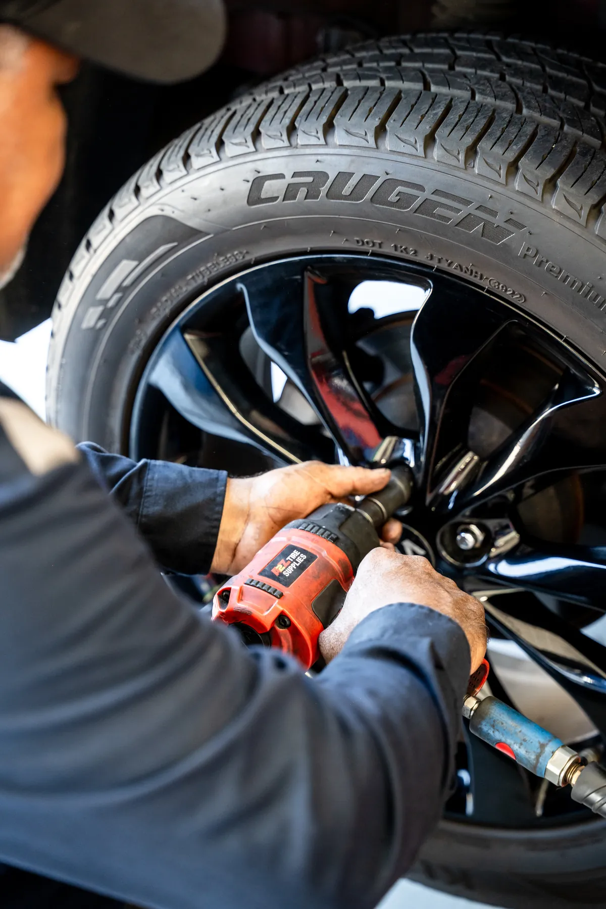 Technician tightening lug nuts on a black alloy wheel with an impact wrench